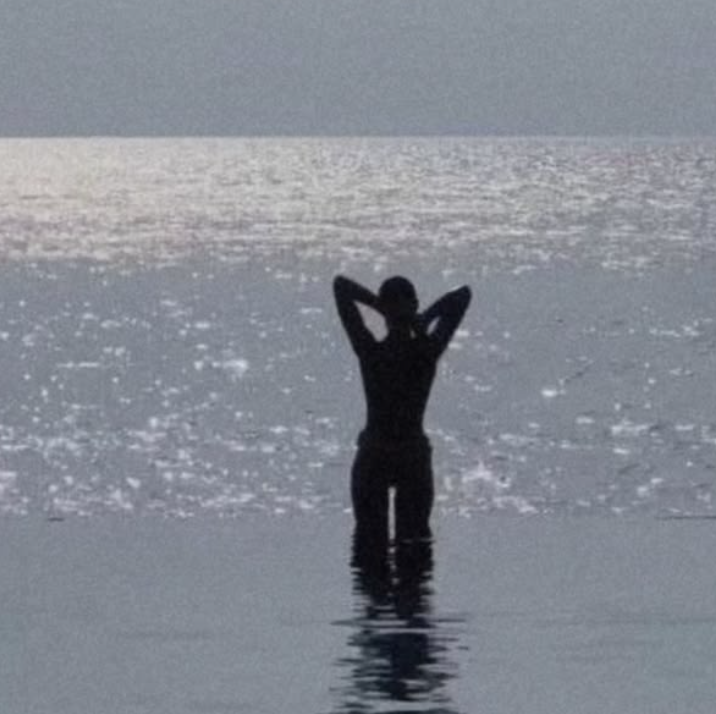 A woman standing in the ocean beneath shimmering sunlight